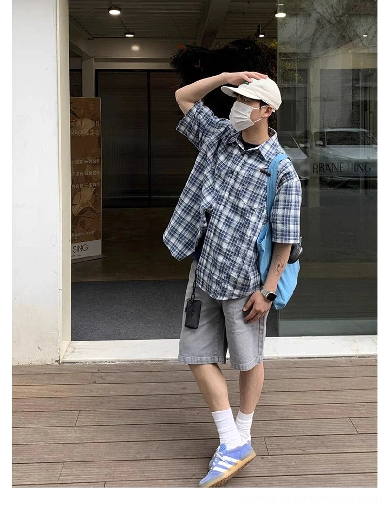 Side streetwear outfit view featuring an oversized blue and white plaid short sleeve shirt, beige cap, blue tote bag, grey shorts, and casual sneakers
