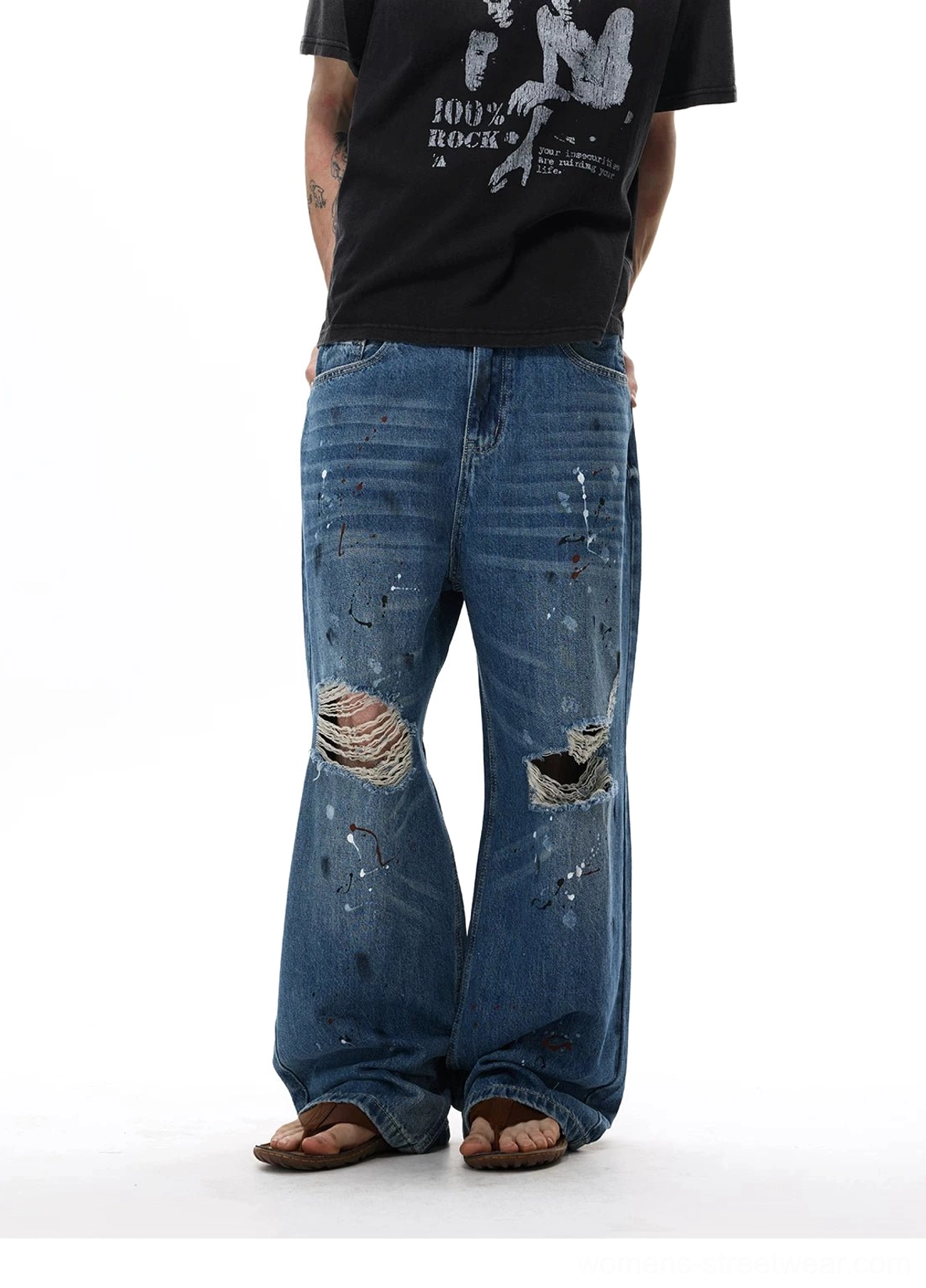 Front view of oversized blue wide-leg jeans with paint splatter details, faded whiskering, and heavily frayed knees