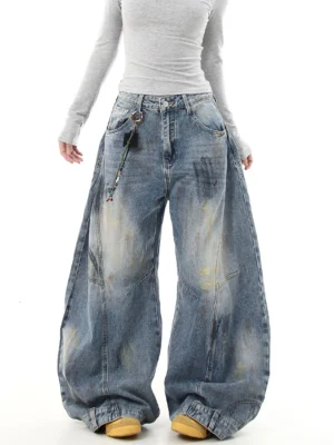Front view of oversized blue wide leg streetwear jeans showing button fly, faded denim wash, attached decorative chain, and relaxed baggy silhouette
