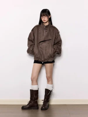 Model wearing an oversized brown faux suede moto jacket with black shorts white knee-high socks and brown boots in a studio