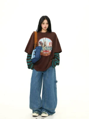 Slight side front view of a relaxed oversized brown retro graphic tee with visible striped cuffs and layered long-sleeve streetwear styling