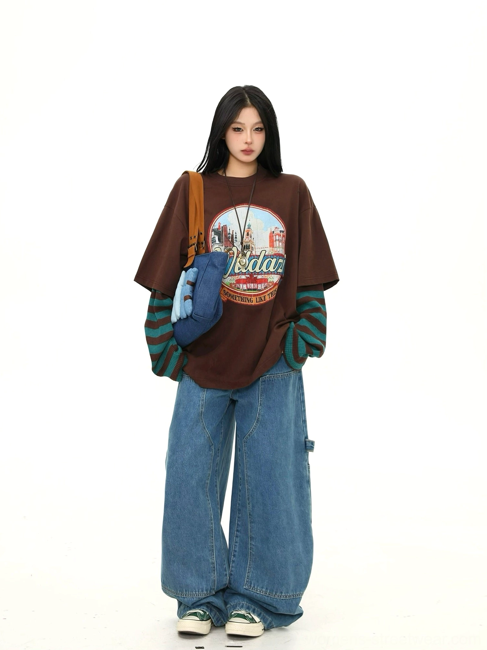 Slight side front view of a relaxed oversized brown retro graphic tee with visible striped cuffs and layered long-sleeve streetwear styling