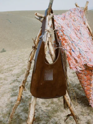 Brown suede and canvas oversized commuter tote bag hanging outdoors with adjustable shoulder strap and side tassel details