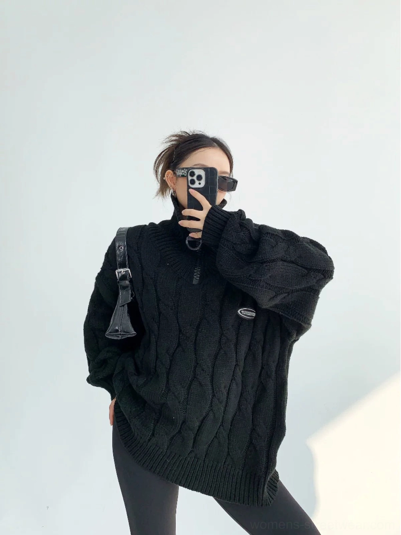 Black oversized cable knit quarter-zip sweater close-up showing textured twisted stitches and chest appliqué