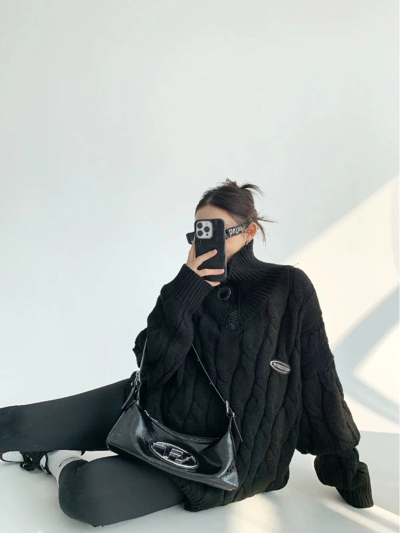 Black oversized cable knit quarter-zip sweater worn in a relaxed seated streetwear outfit