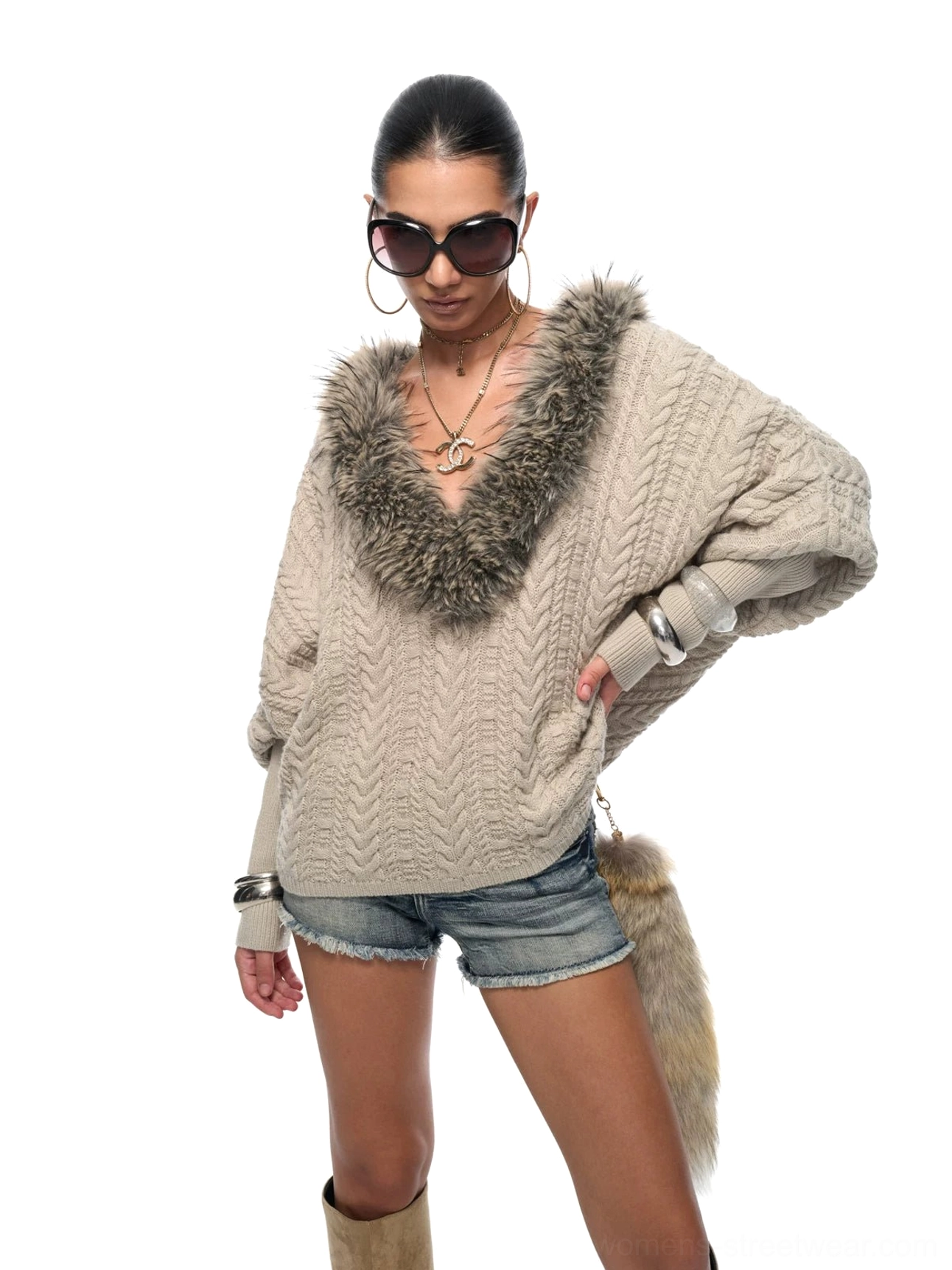 Left side view of an oversized cable knit sweater with faux fur collar, uneven hem, ribbed cuffs, and layered silver accessories