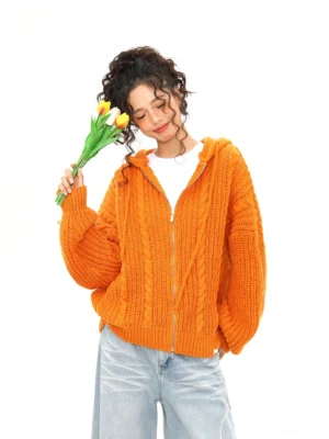 Orange oversized cable knit zip hoodie worn by female model holding tulips in a white studio