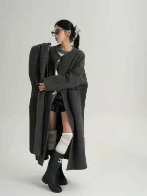 Left three-quarter view of an oversized charcoal grey wool cocoon coat with longline silhouette, dropped shoulders, wide sleeves, and matching sculptural scarf panel