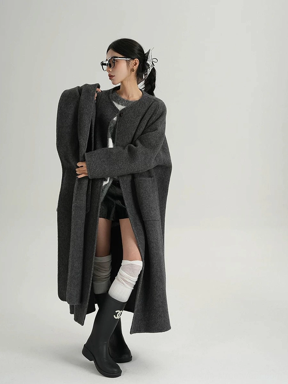 Left three-quarter view of an oversized charcoal grey wool cocoon coat with longline silhouette, dropped shoulders, wide sleeves, and matching sculptural scarf panel