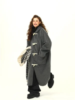 Female model wearing oversized charcoal gray wool-blend hooded duffle coat with white toggle closures, patch pockets, black wide-leg jeans and platform boots