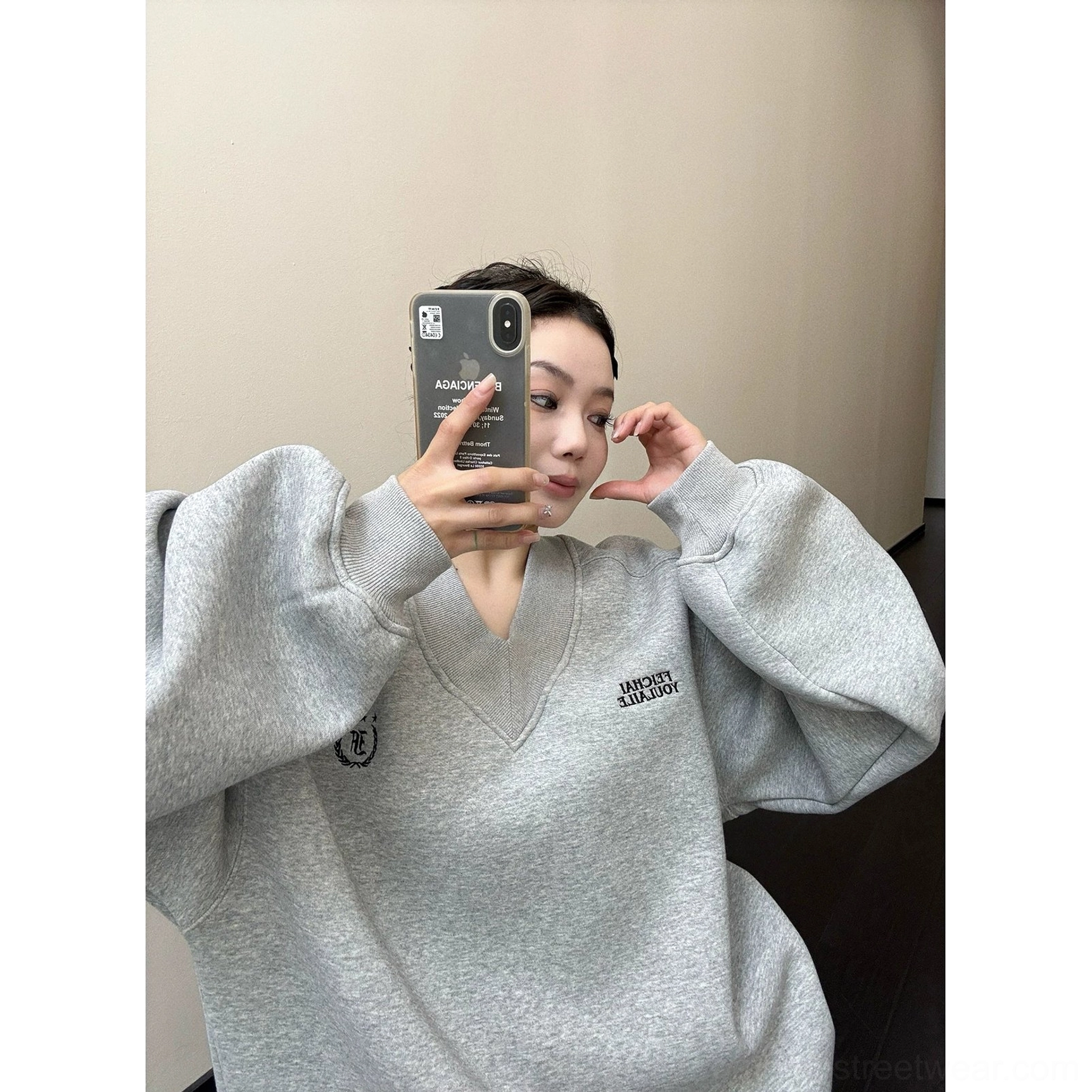 Close-up of gray oversized V-neck fleece sweatshirt showing embroidered chest lettering and crest badge