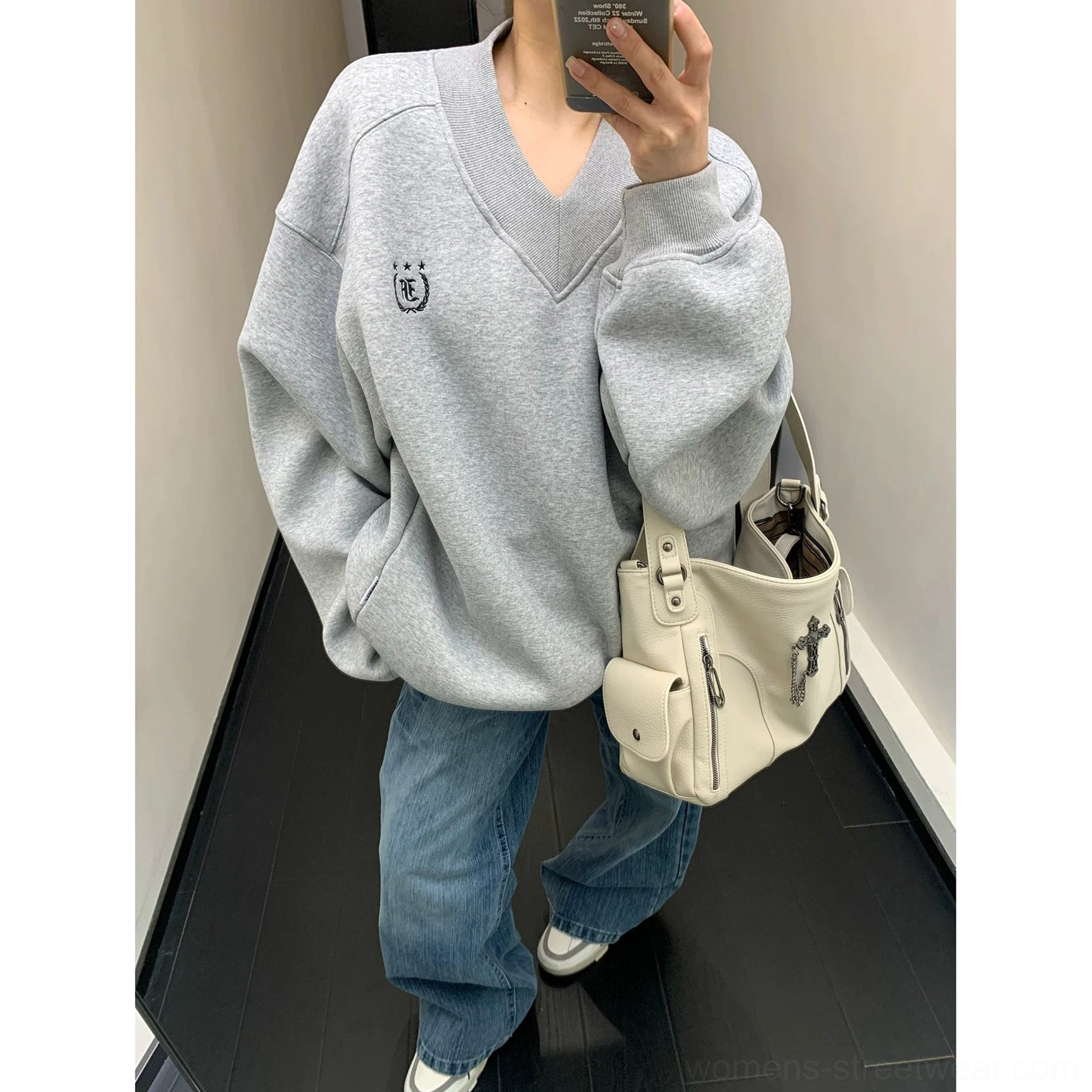 Gray collegiate crest V-neck sweatshirt styled with blue wide-leg denim, white sneakers, and tote bag