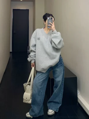 Full body view of heather gray oversized V-neck fleece sweatshirt with wide-leg blue jeans and white sneakers
