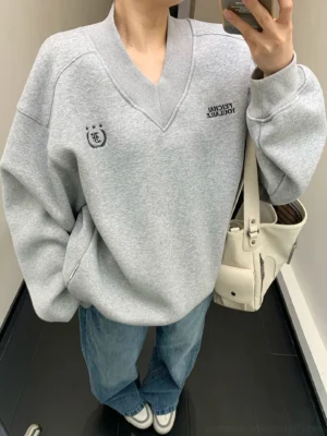 Heather gray oversized collegiate crest V-neck fleece sweatshirt worn with blue jeans in mirror close-up