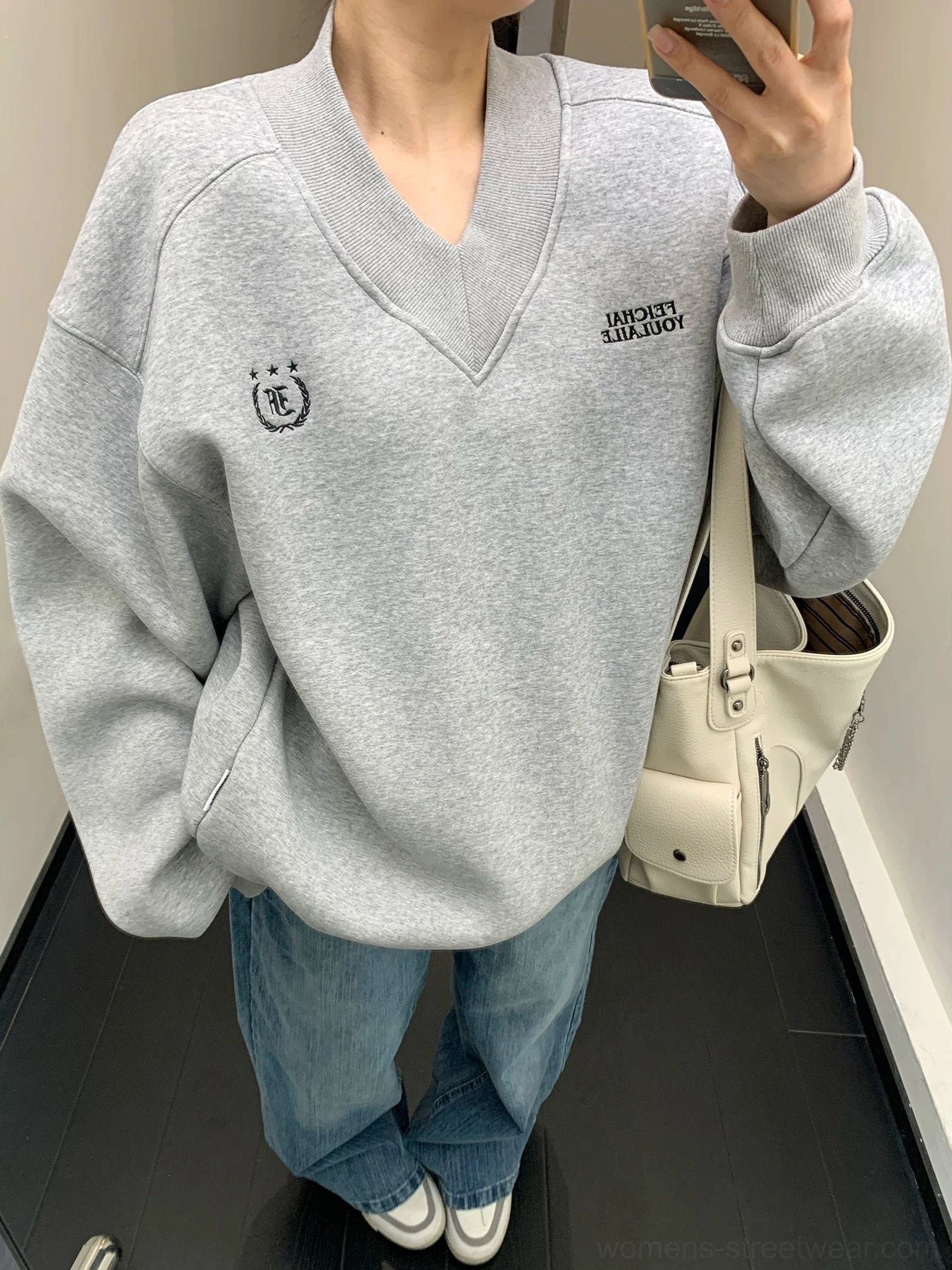 Heather gray oversized collegiate crest V-neck fleece sweatshirt worn with blue jeans in mirror close-up