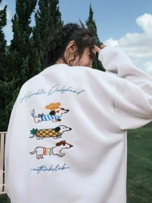 White oversized dachshund graphic sweatshirt shown from the rear three-quarter view with three colorful embroidered-style dogs and handwritten lettering