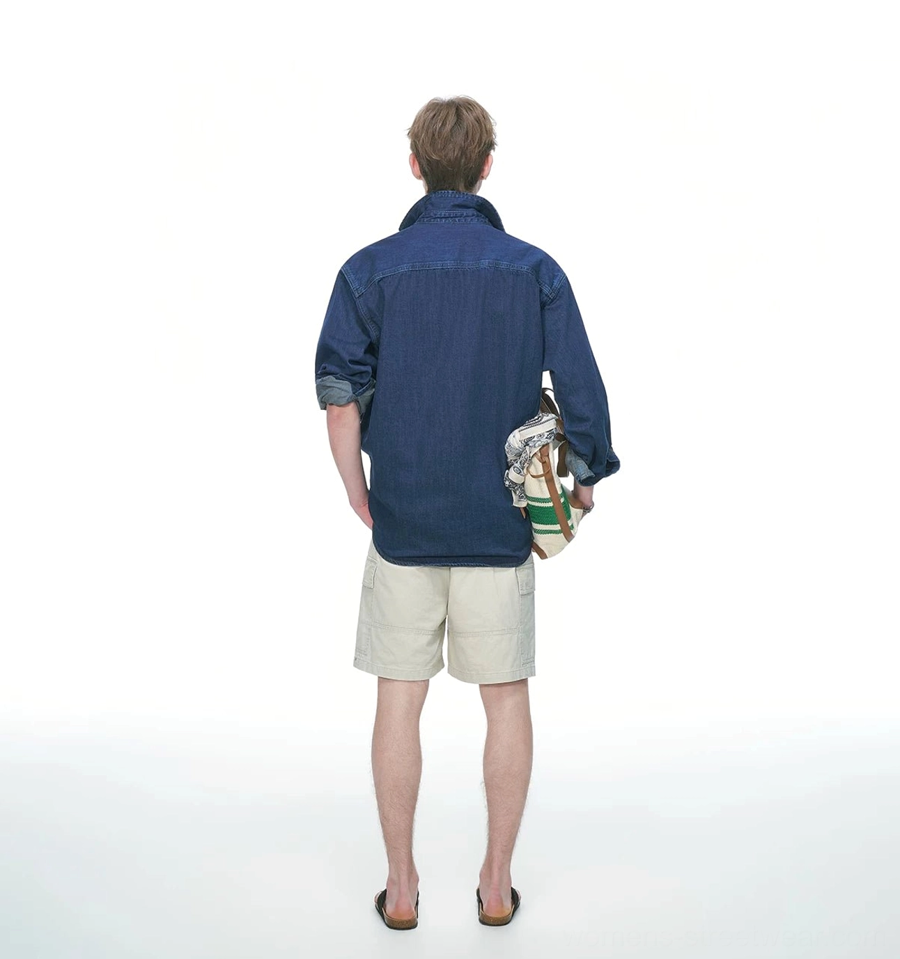 Back view of an oversized dark blue denim shirt showing the back yoke seam, relaxed silhouette, rolled cuffs, and canvas bag styling