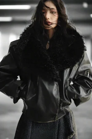 Female model wearing an oversized dark brown faux fur aviator jacket with a plush shearling collar in an industrial streetwear setting