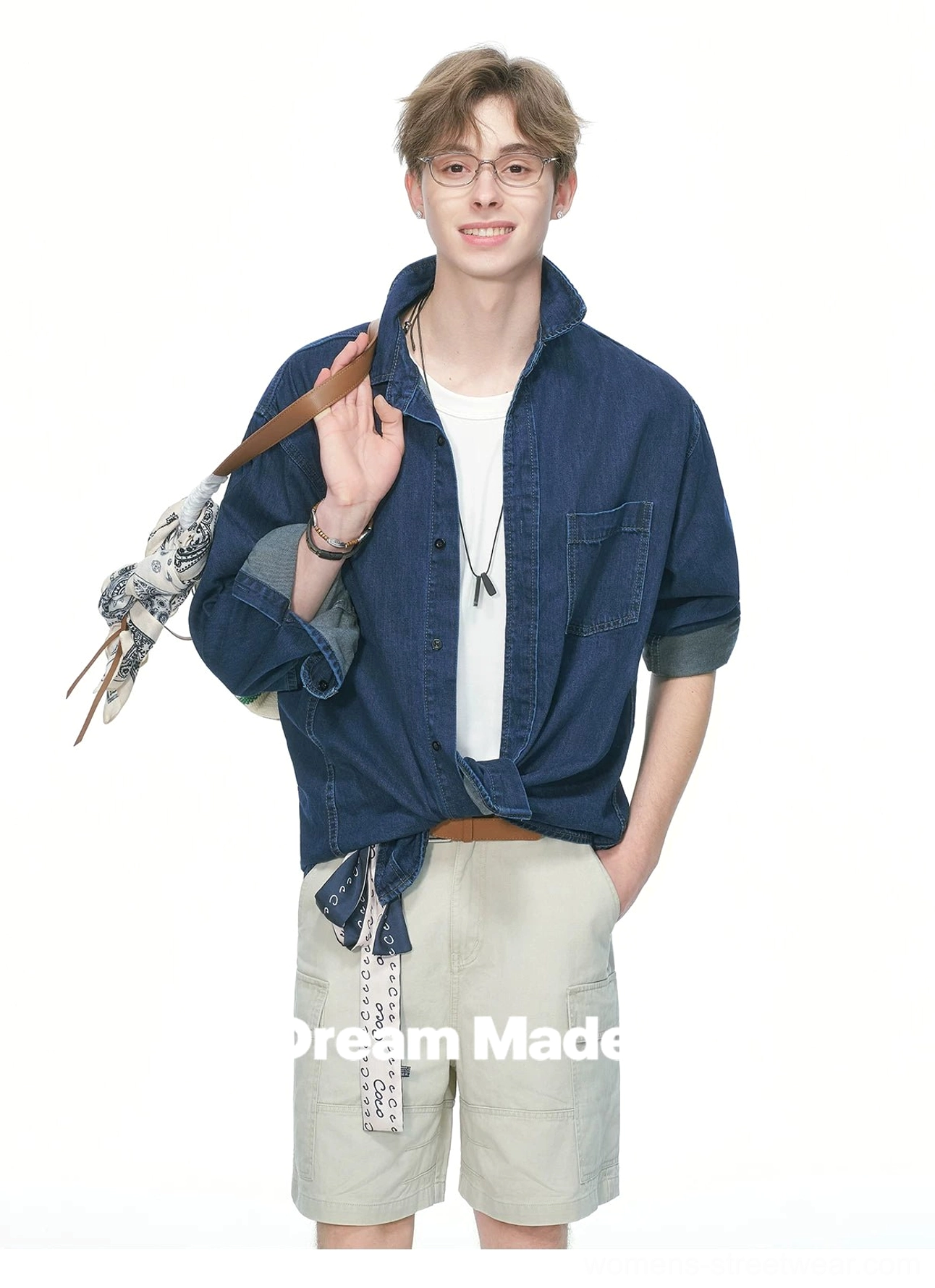 Male model styling an oversized dark denim shirt tied at the hem for a cropped streetwear silhouette with rolled cuffs