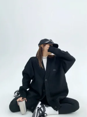 Black oversized button-front knit cardigan in relaxed Korean streetwear styling side sitting studio view