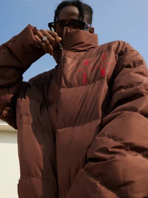 Close-up view of a brown oversized quilted duck-down puffer jacket with high stand collar and embroidered streetwear lettering