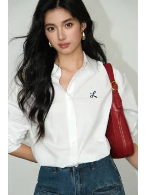 White oversized embroidered button-down shirt styled with blue jeans and red shoulder bag