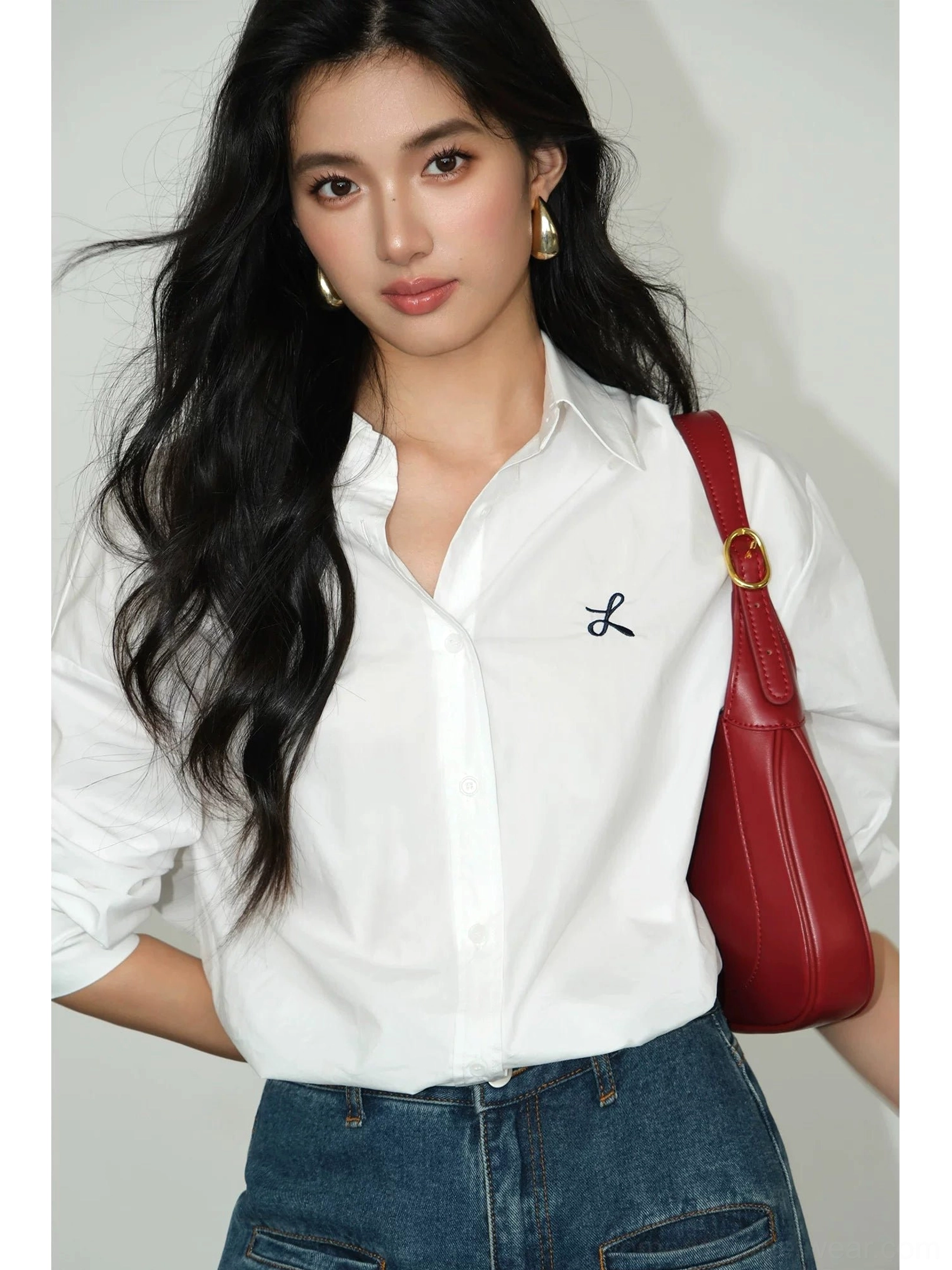 White oversized embroidered button-down shirt styled with blue jeans and red shoulder bag