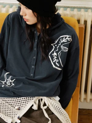 Black oversized embroidered graphic Henley polo shirt with hand-drawn animal and star embroidery styled with a newsboy cap