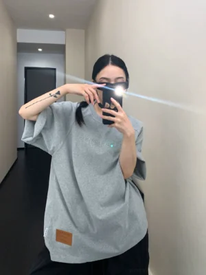 Back view of heather gray oversized embroidered text tee with dropped shoulders and brown lower hem patch