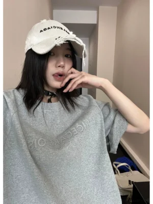 Heather gray oversized embroidered text tee front close-up styled with a distressed white baseball cap and black choker