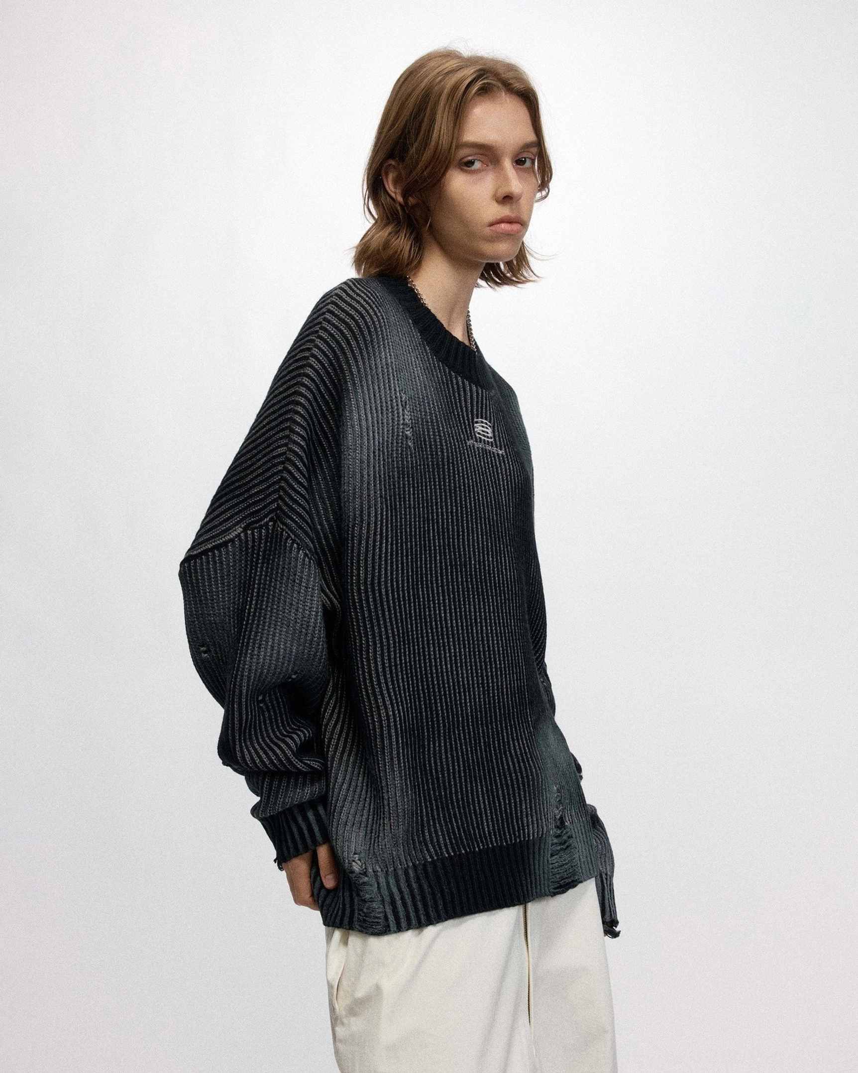 Three-quarter side view of a model wearing an oversized faded black distressed ribbed logo sweater