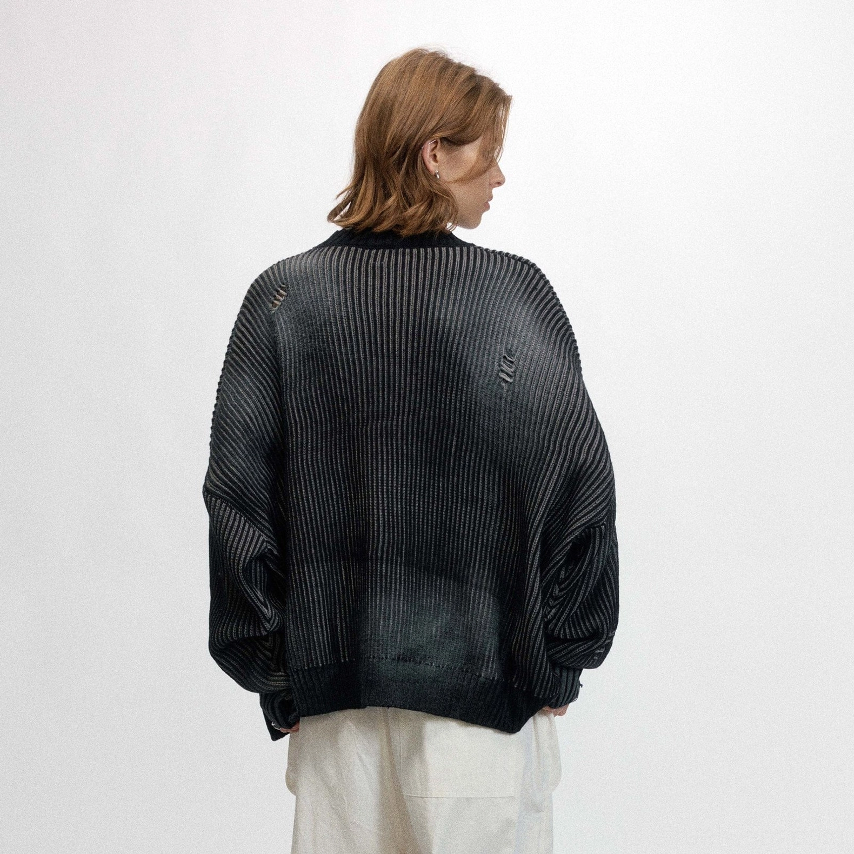Back view of a model wearing an oversized faded black ribbed streetwear sweater with a relaxed drop shoulder silhouette