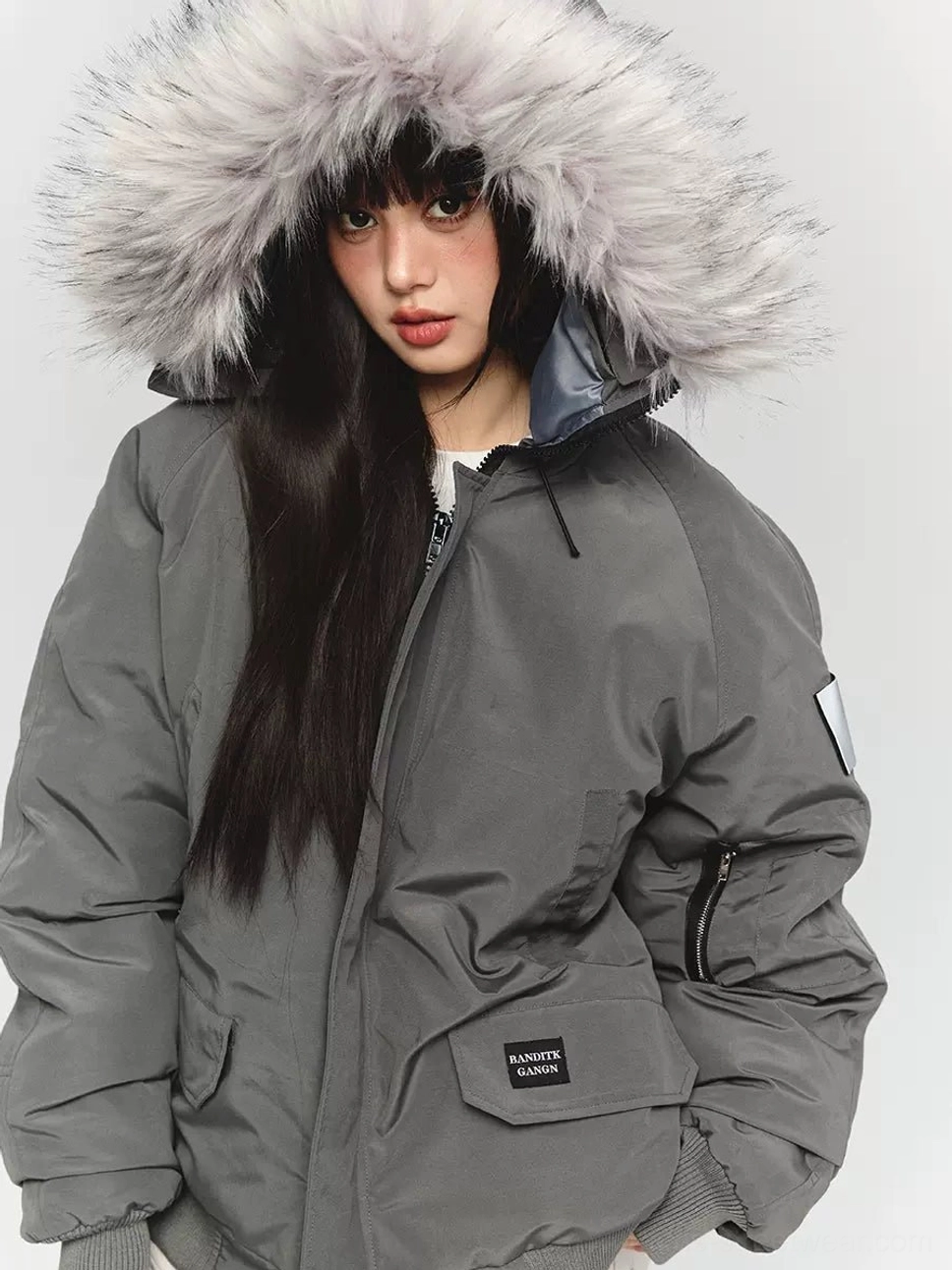 Close-up front view of an oversized dark gray faux fur hooded parka jacket with ribbed cuffs utility pockets and sleeve patch for Korean gorpcore streetwear