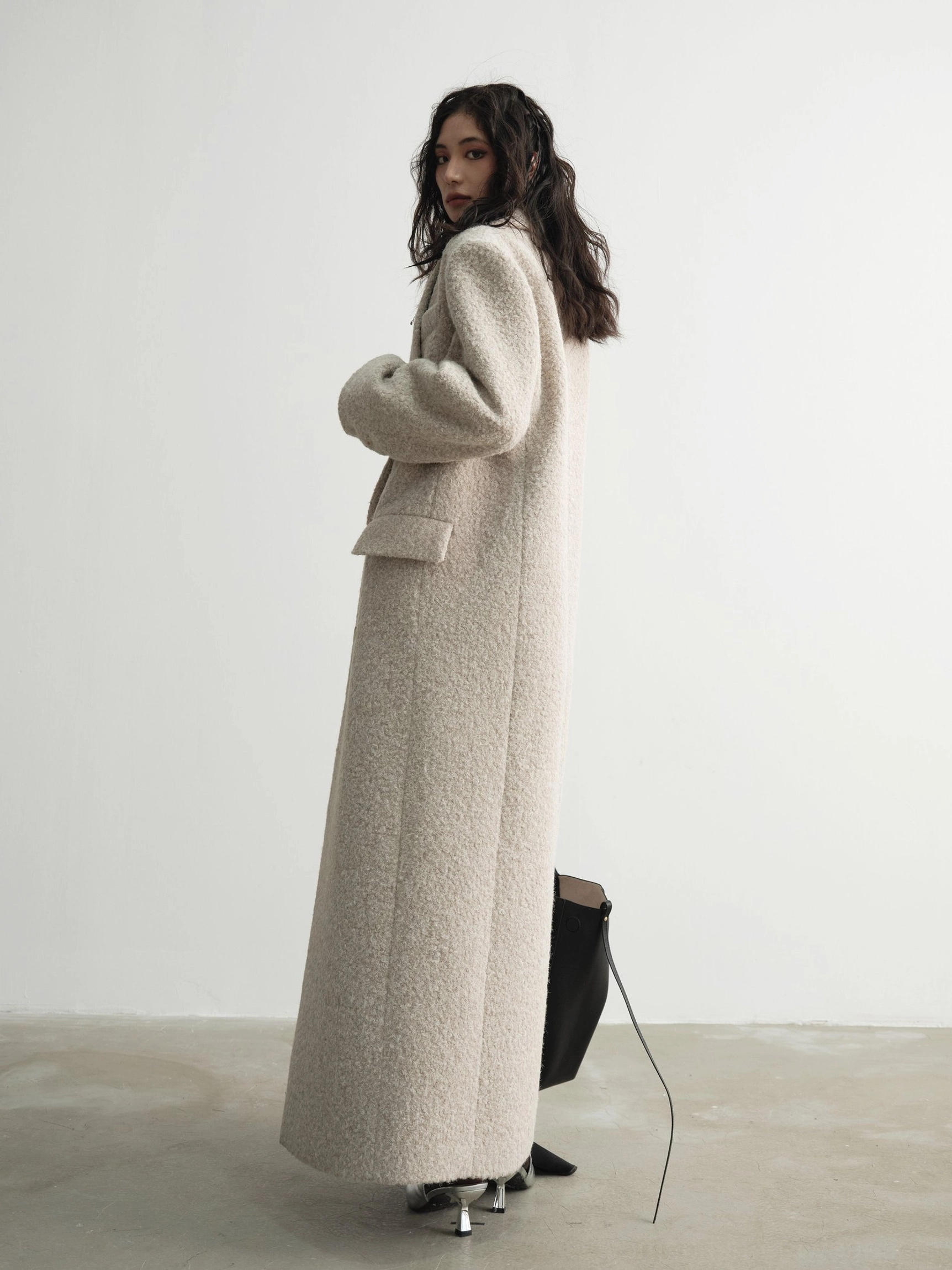 Side back view of a relaxed oversized floor-length wool coat with long tailored sleeves and clean back design