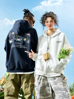 Two streetwear models wearing oversized floral embroidered zip-up hoodies in Dark Blue and White Ash with bold botanical back graphics and butterfly details