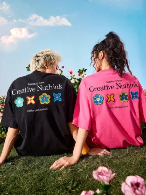 Black and rose red oversized floral patch graphic T-shirts shown from the back on seated models in a sunny flower field