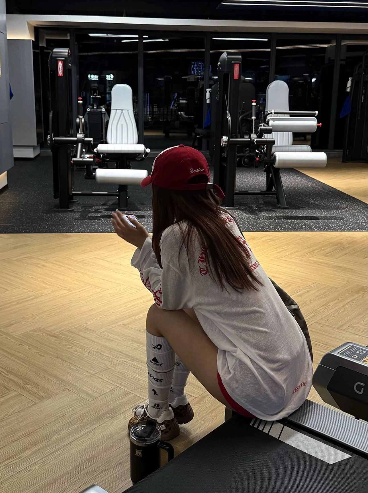 Side back view of an oversized white gothic gym-inspired long-sleeve tee with red printed sleeves and low-rise red athletic shorts