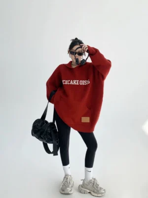 Burgundy oversized graphic knit hoodie with retro chest lettering, kangaroo pocket, long sleeves, black leggings, and chunky sneakers