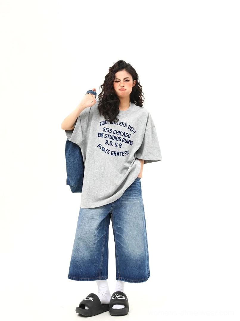 Three-quarter view of oversized heather gray Chicago graphic tee styled with baggy blue denim jeans and tote bag