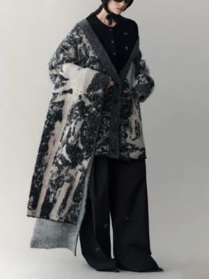 Side view of a relaxed oversized gray wool-blend cardigan with abstract ink print, long matching scarf, black top, and wide-leg pants