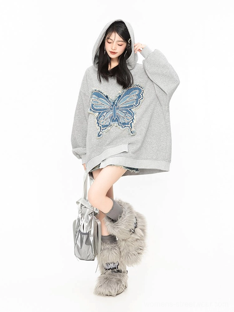 Three-quarter side view of a relaxed oversized grey butterfly hoodie with frayed denim appliqué and asymmetric hem