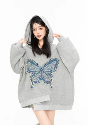 Close-up front view of an oversized grey butterfly hoodie with frayed blue denim appliqué, dropped shoulders, long sleeves, and asymmetric hem