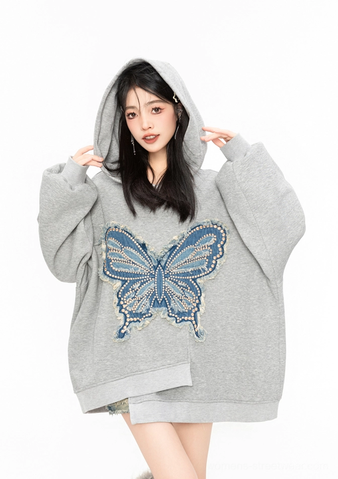 Close-up front view of an oversized grey butterfly hoodie with frayed blue denim appliqué, dropped shoulders, long sleeves, and asymmetric hem