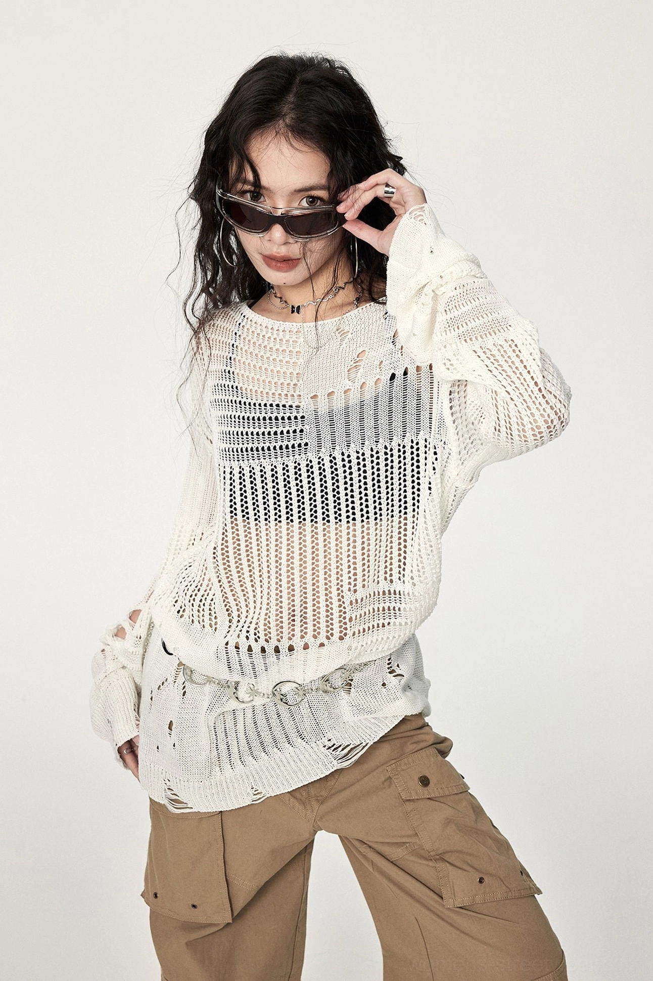 Side front view of an oversized off-white hollow-out crochet sweater with cut-out sleeves, asymmetrical hem, and metal ring waist decoration