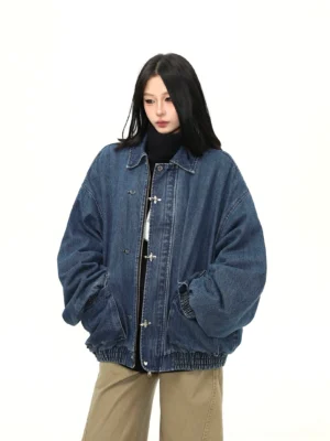Front view of an oversized dark indigo denim bomber jacket for women with metal toggle closures, spread collar, elasticated hem, and side pockets