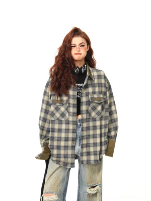 Front full-body view of an oversized khaki and dark blue plaid flannel streetwear shirt with olive green cuffs, worn over a black cropped top with distressed wide-leg jeans