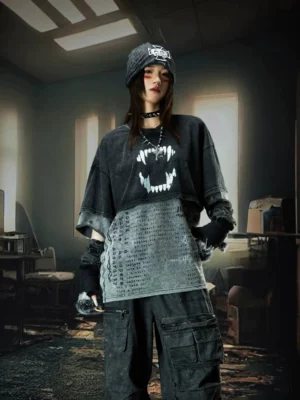 Female model wearing an oversized layered acid wash punk graphic tee with fanged mouth print and deconstructed hem in an industrial streetwear setting