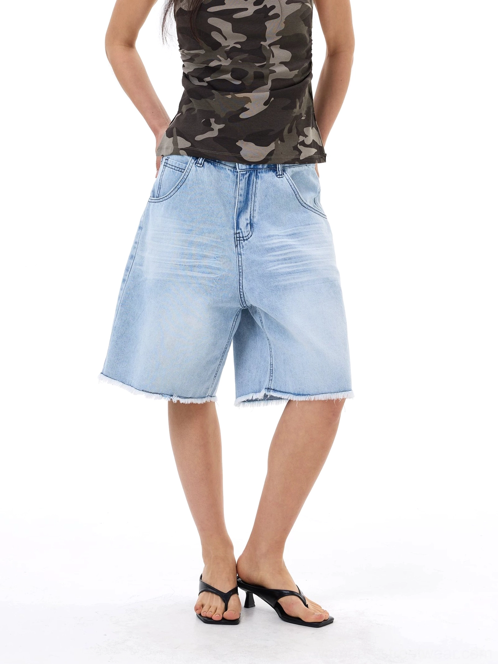 Back view of oversized light blue denim Bermuda shorts with faded finish, zipper fly construction, and raw edge hems
