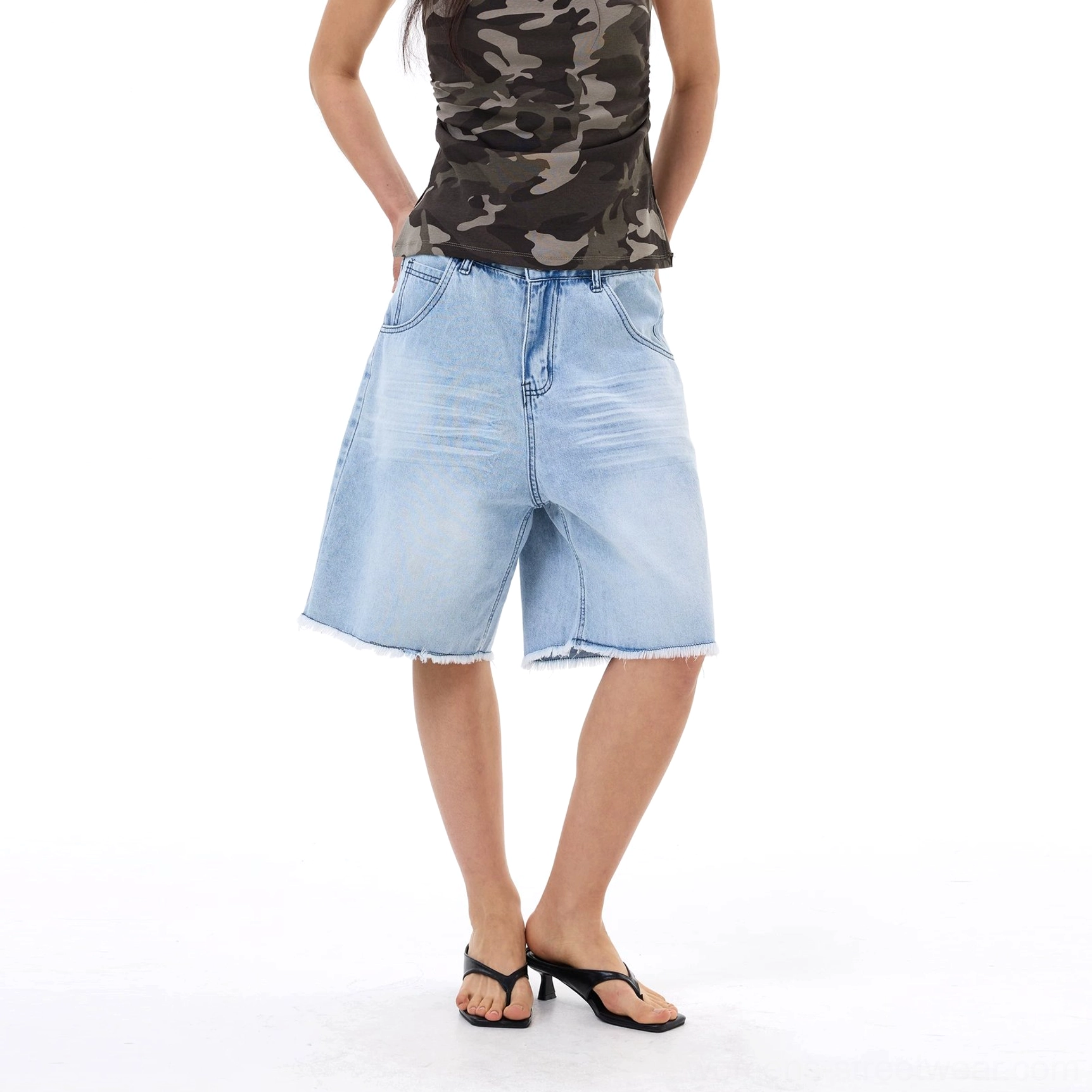 Three-quarter front view of oversized light wash denim Bermuda shorts with extra relaxed fit and frayed raw bottom hem