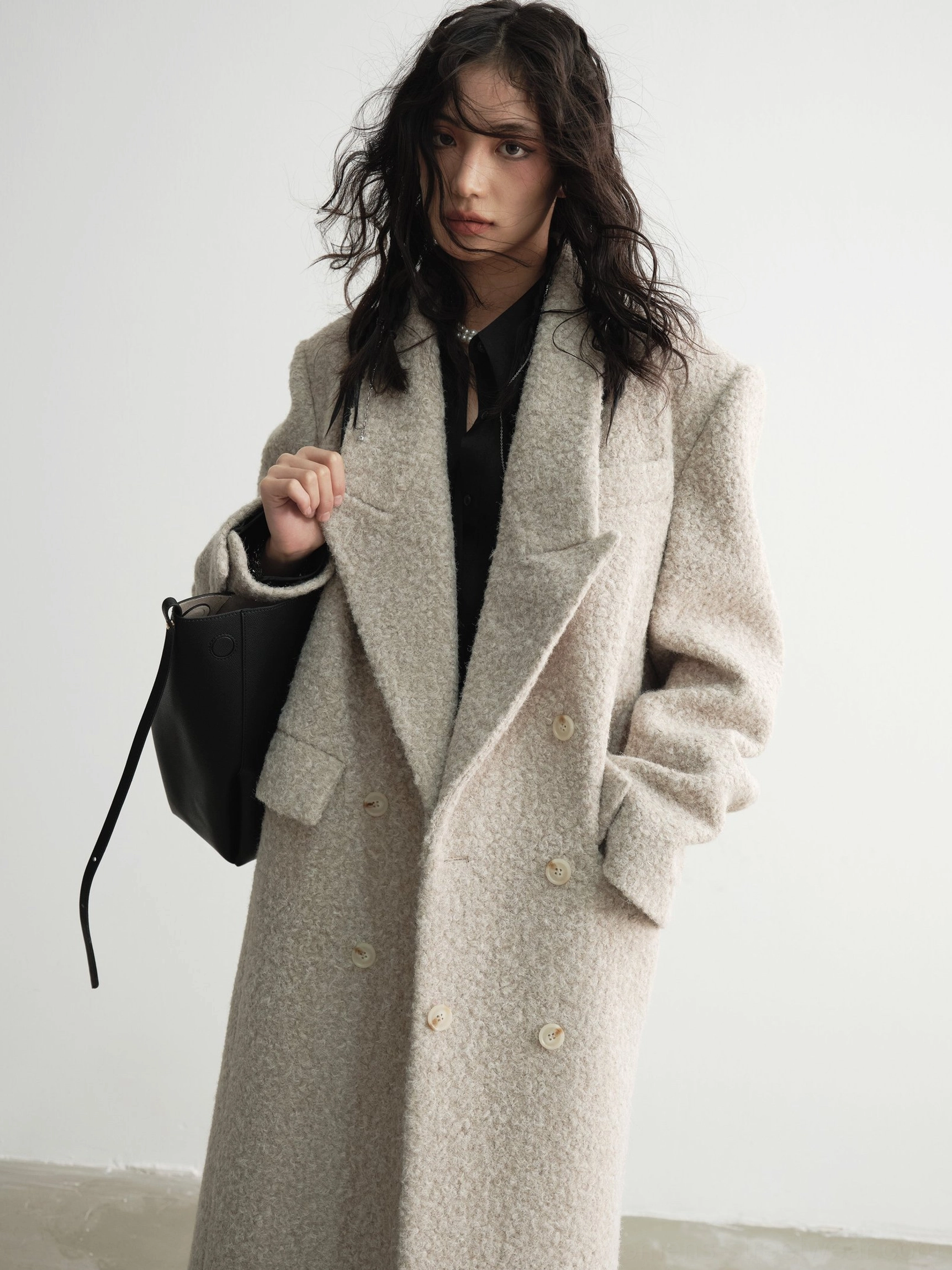 Three-quarter view of an oversized oatmeal beige bouclé maxi coat with front slip pockets and relaxed streetwear silhouette